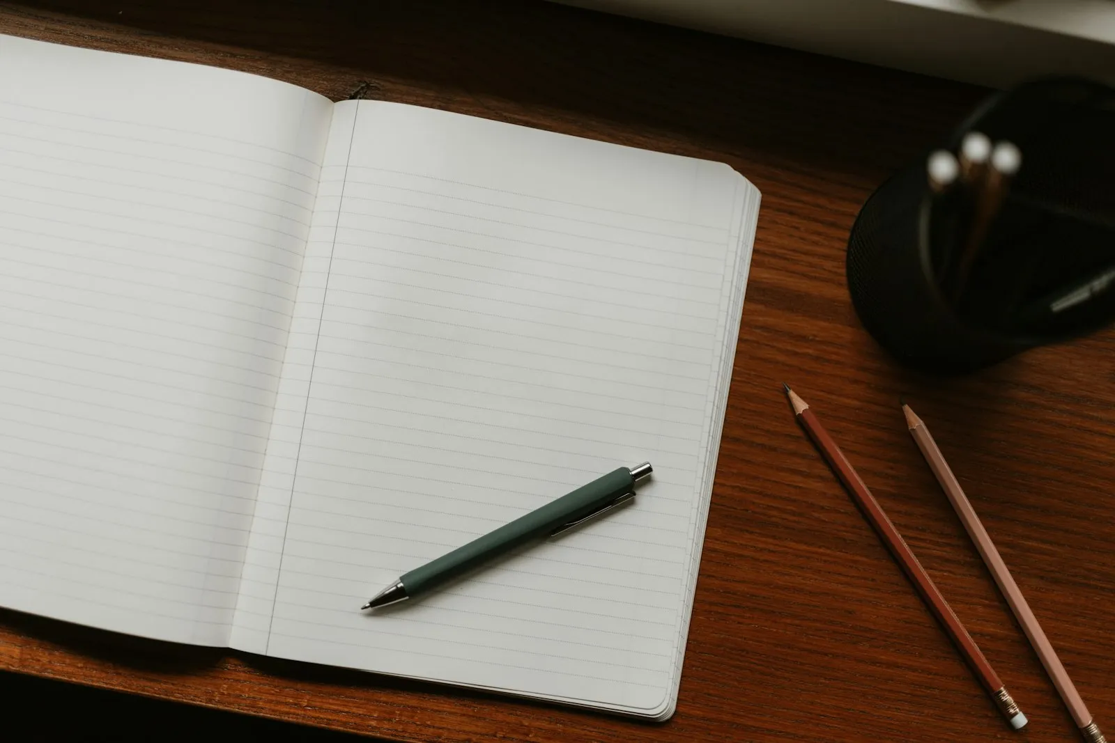 An open notebook with pen and pencils on a desk